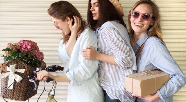 3 jeunes femmes posant sur un vélo avec des fleurs et un colis