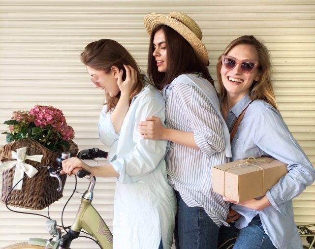 3 jeunes femmes posant sur un vélo avec des fleurs et un colis